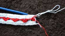 Переворачиваем вязание. Крючок вводим вот таким образом, чтобы захватить красную нить и вытянуть петельку.